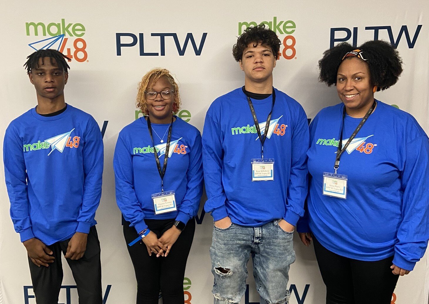 Three teenage students from the KIPP KC Legacy High School team stand to the left of their teacher. All are wearing the same royal blue, long-sleeved shirt and standing in front of a make48 and PLTW banner. 