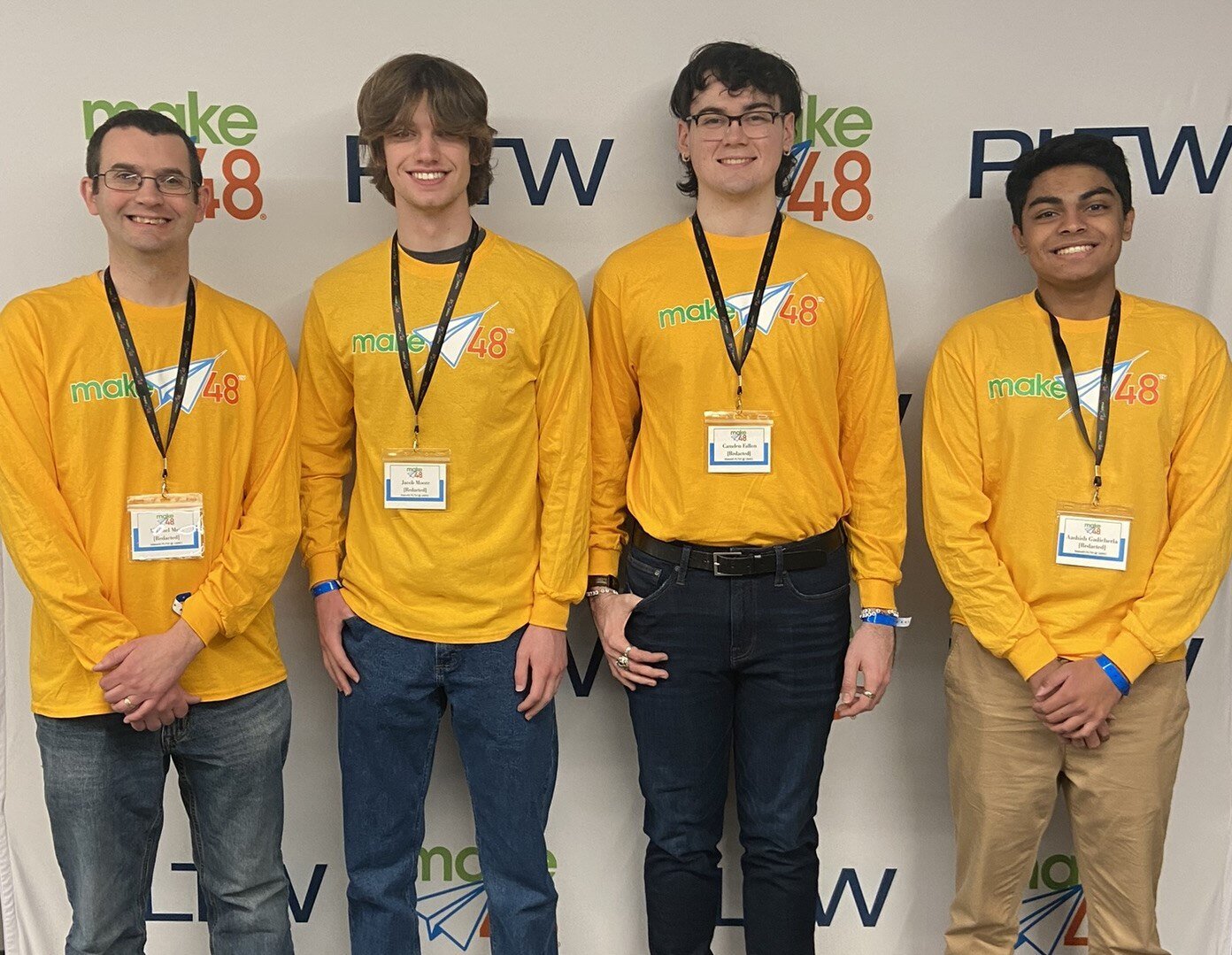 Three teenage students from the Columbia Area Career Center team stand to the right of their teacher for a group photo. All are wearing the same mustard yellow, long-sleeved shirt and standing in front of a make48 and PLTW banner. 