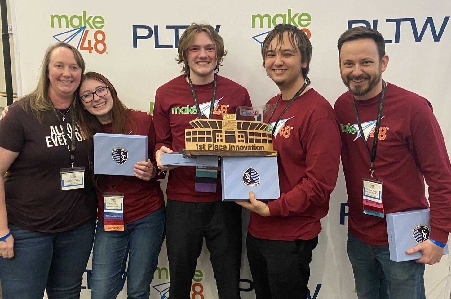 The Innovation Hall Bears team members stand with their teachers on either side, smiling brightly and holding their first place innovation trophy. 